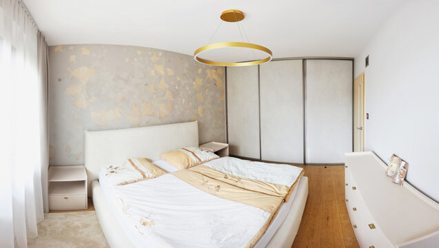 A contemporary bedroom interior with wood paneling, beige bed, armchair, pendant lights, soft curtains, and herringbone parquet flooring.