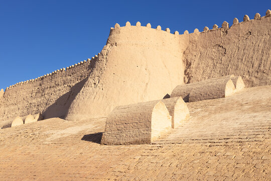 Massive mud-brick fortress walls of Ichan Kala in Khiva with crenellations against a clear blue sky. Ancient Central Asian fortification ideal for travel publications and heritage content.