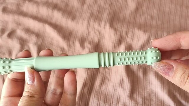 Teether for children in a woman's hand against the background of a crib