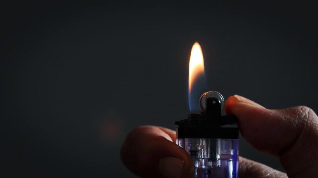 A man lights a lighter. A man holds a lighter in his hand and spins a drum on a dark background. The lighter emits sparks and ignites close up.