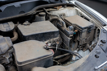 Fototapeta premium Close up of dirty car engine compartment showing fuse box battery and wiring components. Automotive maintenance concept