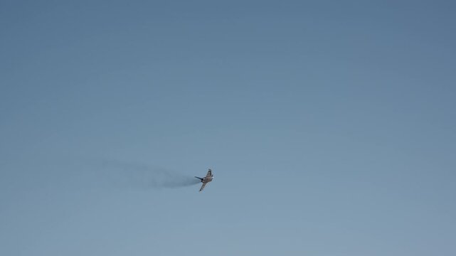 Twin engine combat aircraft banks in steep turn against cloudless blue sky, viewed from ground level in bright daylight