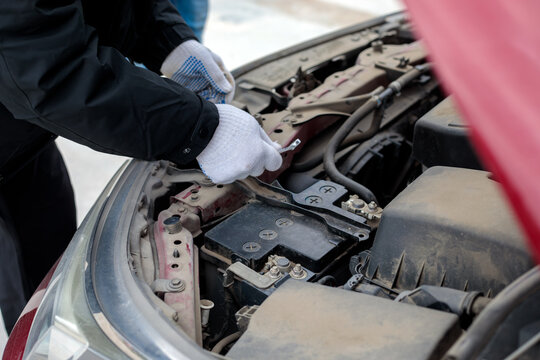 Hands in white gloves replacing or checking car battery in engine compartment under open hood. Car maintenance concept