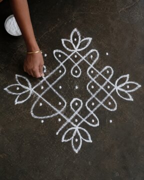 Authentic Close-Up of Indian Woman's Hand Drawing Traditional White Kolam Geometric Pattern on Dark Stone Floor with Rice Powder, Dark Moody Folk Art and Cultural Heritage Ritual Concept
