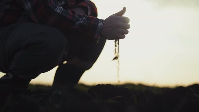 Villager in agricultural fields, closeup view of male hands with pouring soil. Professional agronomist or bioengineering examining ground in farmland, planning sowing, soiling and good harvesting