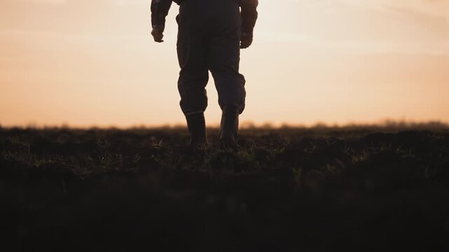 Agricultural and rural lifestyle, villager walking in field in sunset or sunrise . Countryside romantic mood, farmer stepping on soil, back view, details from male legs in rubber shoes to full-length