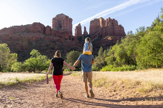 Family of three holding hands outdoors on hiking trail