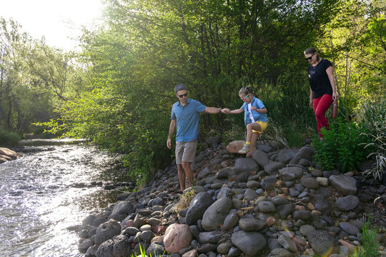 Family of three cautiously approach water on rocky shores