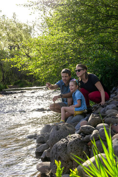 Family of three enjoying outdoor stream on rocky shore