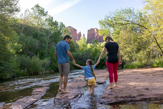 Family of three walking barefoot outdoors in wilderness creek