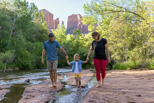 Family of three walking barefoot outdoors by creek