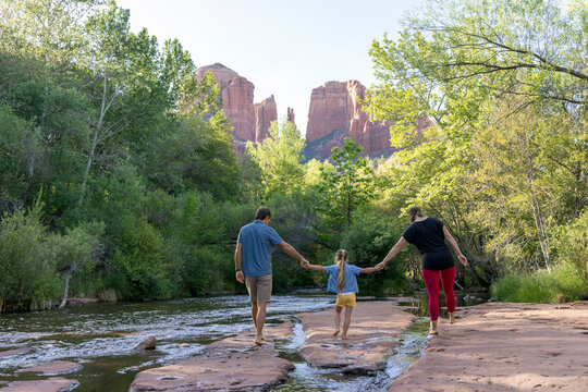 Family of three walk barefoot by wilderness creek