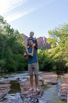 Daughter on dad's shoulders pointing in outdoors by stream