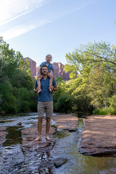 Daughter on shoulders of father outdoors by natural stream