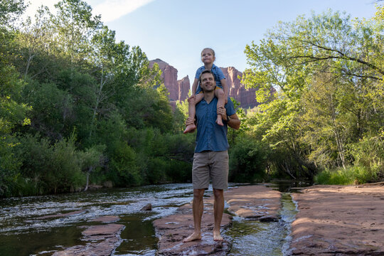 Dad holds daughter on shoulders outdoors by stream