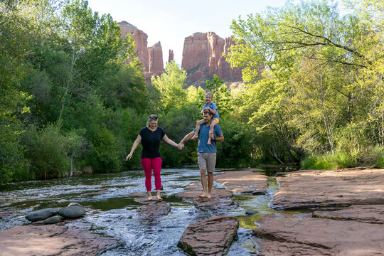 Family of three holding hands outdoors walking in creek