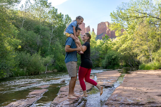 Family of three walking barefoot outdoors around stream