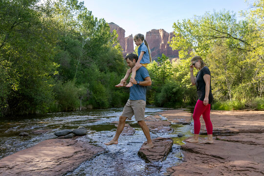 Family of three walking barefoot crossing stream