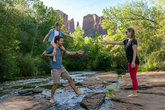 Family of three reaching outdoors over rocky stream