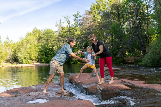 Family of three outdoors crossing rocky stream