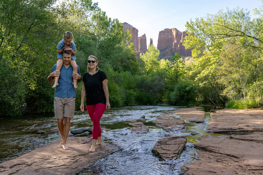 Family of three walk barefoot outdoors by creek