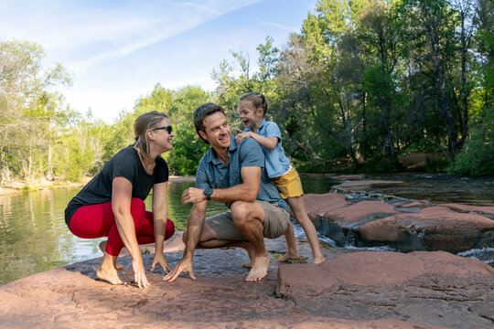Family of three laughing playing outdoors by creek