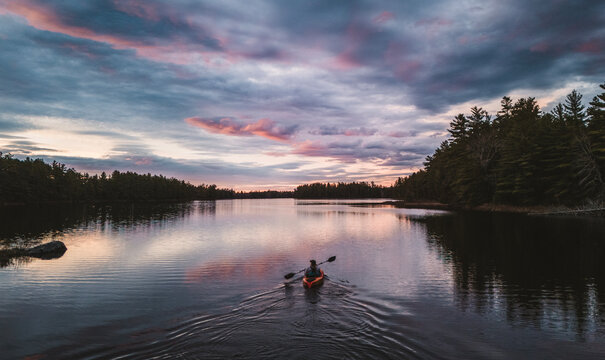 Lone person kayaking on a calm forest lake in Maine woods.
