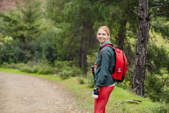 Smiling woman with a red backpack hiking in a forest