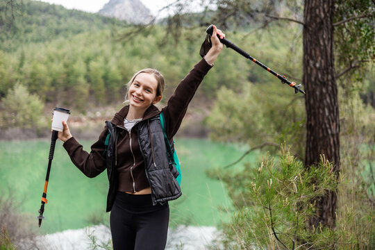 Happy hiker posing with coffee by a lake