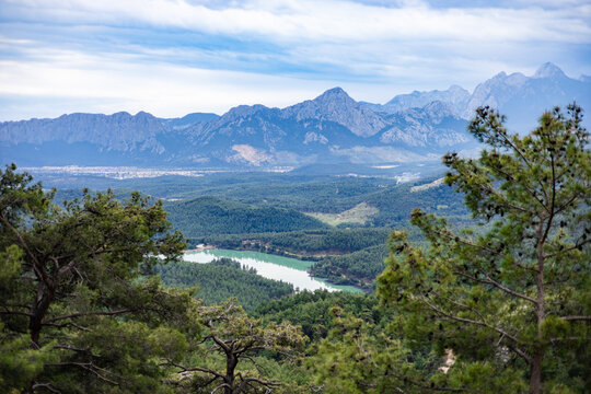 Pine trees framing a vast mountain valley with a lake