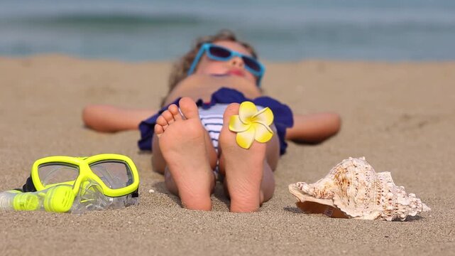A happy child is lying on the sandy beach during the summer vacation