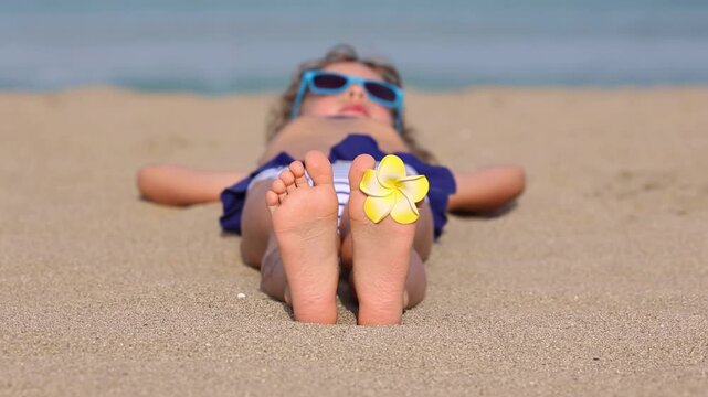A happy child is lying on the sandy beach during the summer vacation