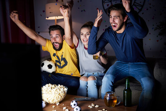 Excited friends sitting on the sofa watching Tv