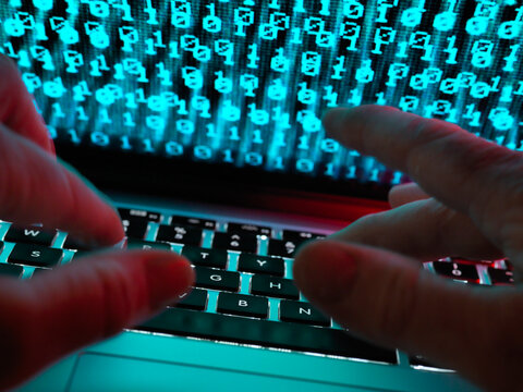 Hacker coding a computer virus infecting a laptop