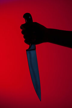 Human hand holding kitchen knife against red background