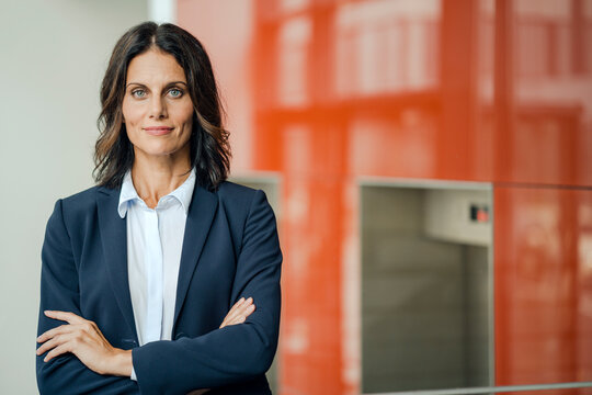 Portrait of a successful businesswoman, standing in front of elevator, with arms crossed