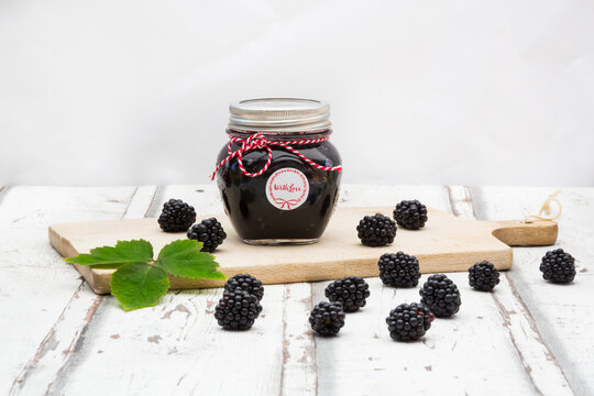 Glass of homemade blackberry jam, blackberries and leaf on wooden board