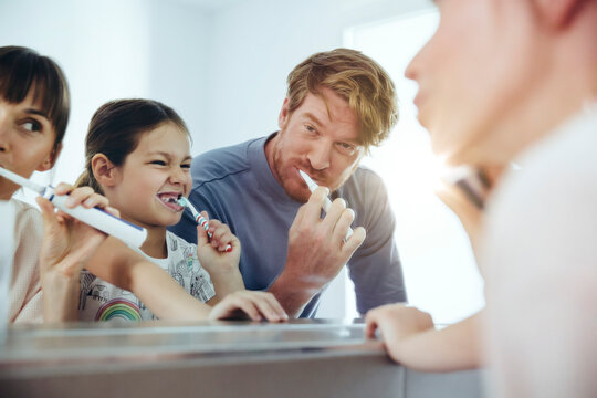 Family of three brushing their teeth in front of big mirror
