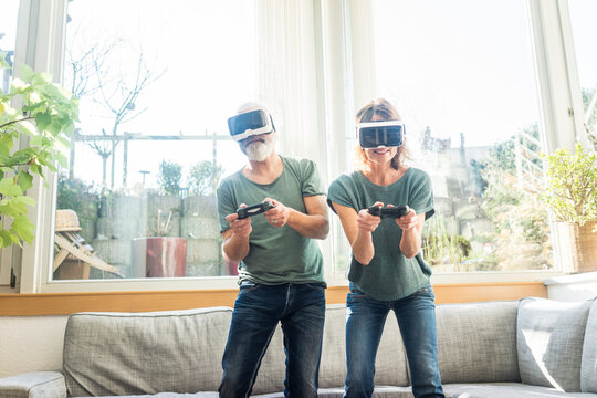 Mature couple in kiving room at home wearing VR glasses playing video game
