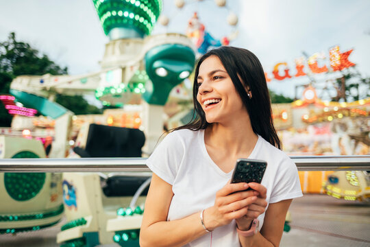 Cheerful young woman holding smart phone looking away at amusement park