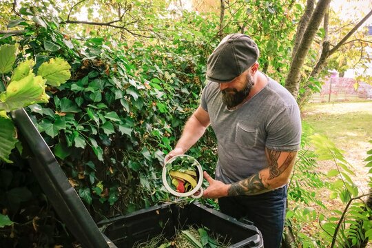 Mature man discarding kitchen scraps on compost pile