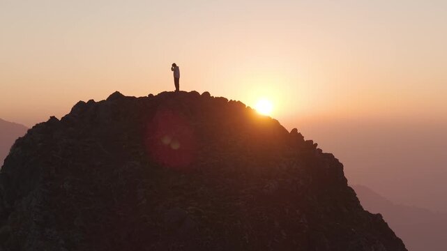 4K aerial drone shot of a boy standing on a rocky mountain cliff during sunrise in Uttarakhand, India.