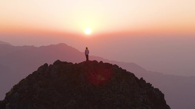 4K drone footage capturing a boy admiring the colorful morning sky from a mountain summit in Uttarakhand.