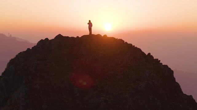 4K drone shot of a lone boy standing on a mountain cliff with vibrant sunrise colors in the Himalayan sky.