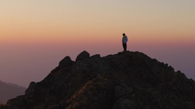 4K aerial footage of a traveler standing on a rocky peak watching the sun rise over the Himalayas in Uttarakhand.