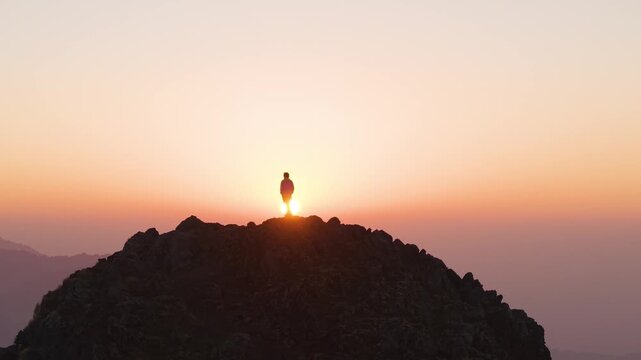 4K morning sunrise drone shot of a boy standing peacefully on a Himalayan cliff in Uttarakhand, India.