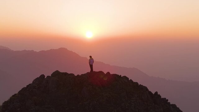 4K scenic aerial footage of a traveler overlooking vibrant sunrise skies from a rocky mountain top in Uttarakhand.