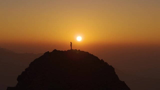 4K aerial cinematic view of a boy enjoying golden sunrise light atop a rocky mountain in Uttarakhand.