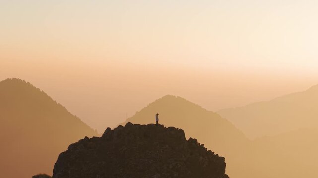 4K scenic drone footage of a traveler enjoying the Himalayan sunrise from a rocky summit in Uttarakhand.