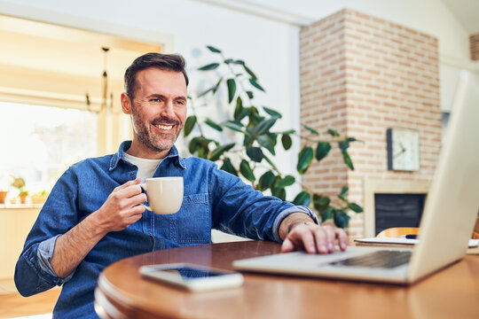Man drinking coffee and working on laptop at home